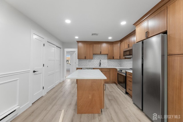 kitchen featuring appliances with stainless steel finishes, baseboard heating, a kitchen island, light wood finished floors, and recessed lighting