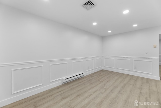 empty room featuring a baseboard radiator, recessed lighting, light wood finished floors, a decorative wall, and a wainscoted wall