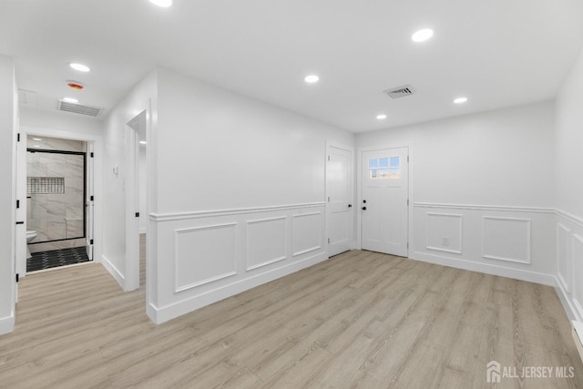 unfurnished room featuring light wood finished floors, recessed lighting, wainscoting, and a decorative wall