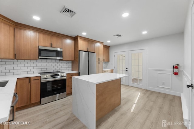 kitchen featuring stainless steel appliances, french doors, light wood-type flooring, tasteful backsplash, and brown cabinetry