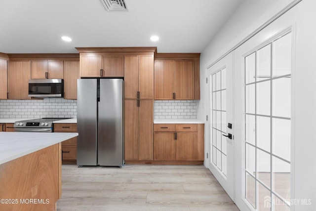 kitchen with appliances with stainless steel finishes, brown cabinetry, backsplash, light wood-type flooring, and recessed lighting