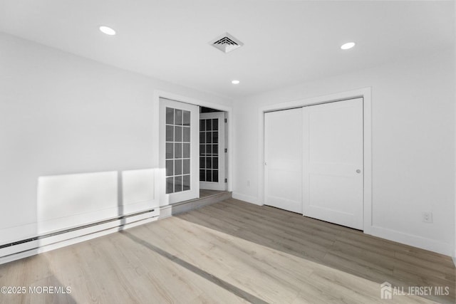 unfurnished bedroom with baseboard heating, wood finished floors, baseboards, recessed lighting, and a closet
