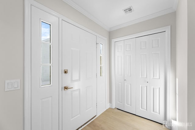 foyer with light wood-style floors, visible vents, and crown molding