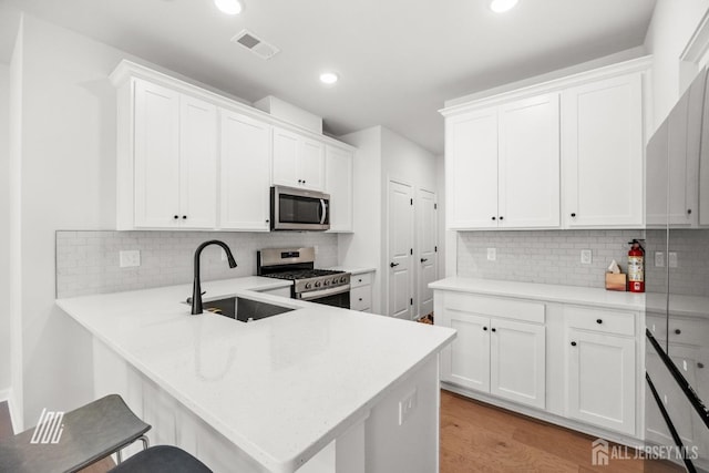 kitchen featuring kitchen peninsula, white cabinetry, sink, and appliances with stainless steel finishes