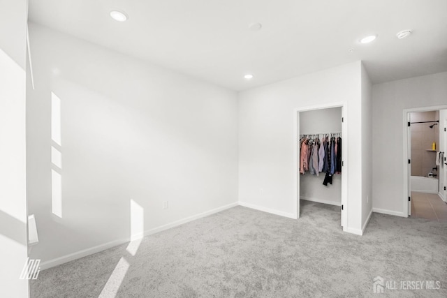 unfurnished bedroom featuring a spacious closet, a closet, and light carpet