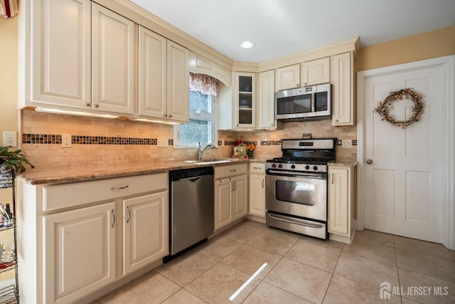 kitchen featuring appliances with stainless steel finishes, cream cabinets, a sink, tasteful backsplash, and light tile patterned floors