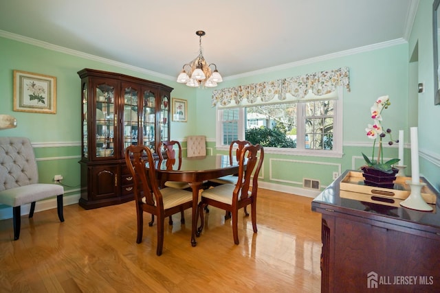 dining area with a chandelier, crown molding, and light wood-style flooring