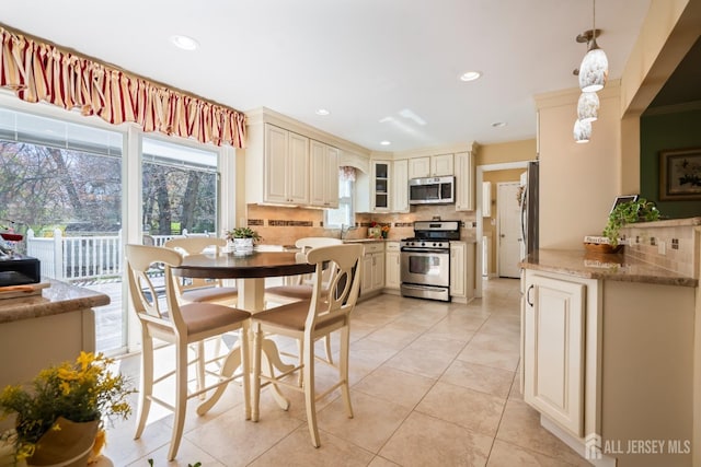 kitchen featuring appliances with stainless steel finishes, cream cabinetry, tasteful backsplash, light tile patterned floors, and glass insert cabinets