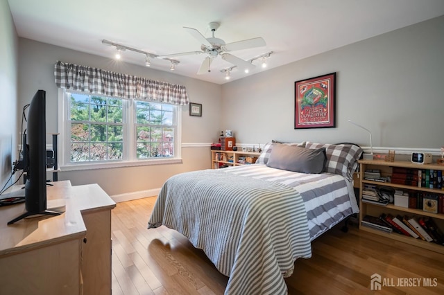 bedroom featuring rail lighting, light wood-style flooring, baseboards, and a ceiling fan