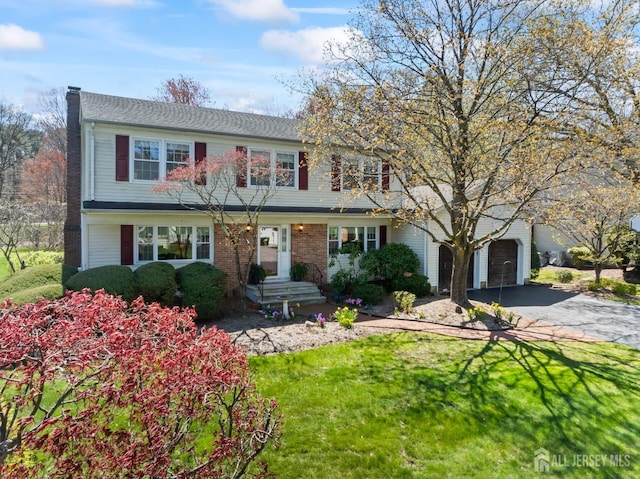colonial inspired home with a garage, a chimney, asphalt driveway, and a front lawn