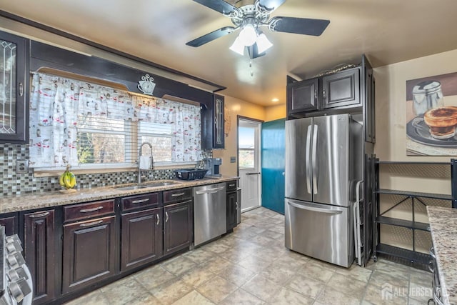 kitchen featuring sink, dark brown cabinets, appliances with stainless steel finishes, light stone countertops, and decorative backsplash