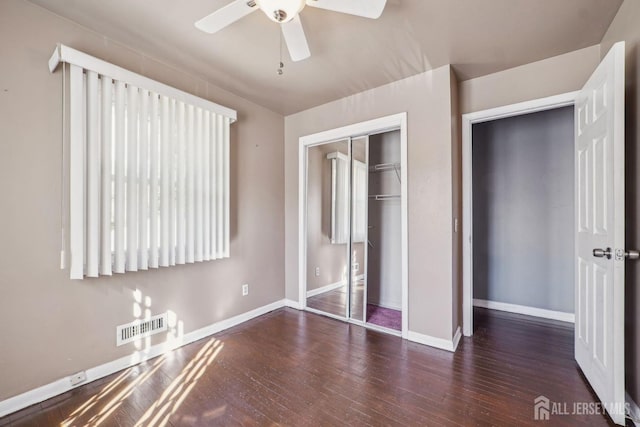 unfurnished bedroom with dark wood-style floors, a closet, visible vents, and baseboards