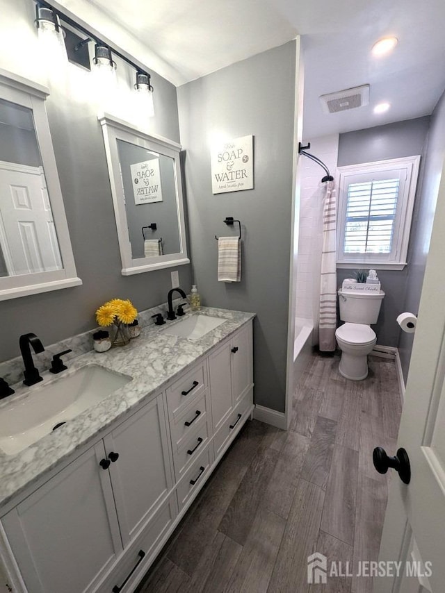 bathroom featuring a sink, visible vents, double vanity, and wood finished floors