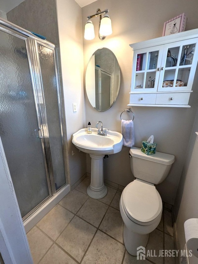 bathroom featuring a shower stall, baseboards, tile patterned flooring, and toilet