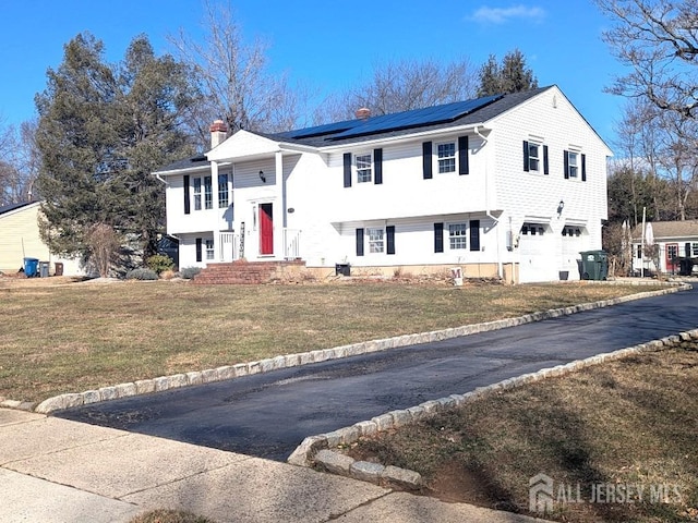 split foyer home featuring solar panels, driveway, an attached garage, and a front yard