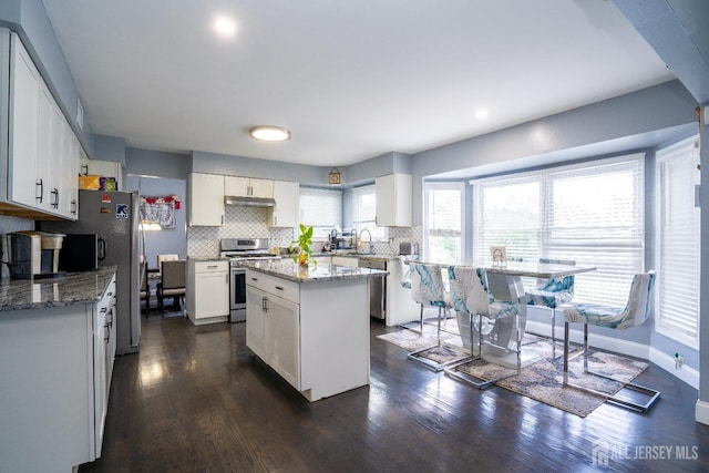 kitchen featuring stainless steel range with gas cooktop, decorative backsplash, dark wood-type flooring, under cabinet range hood, and white cabinetry