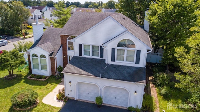 view of front of home with driveway, roof with shingles, a front yard, a garage, and a chimney