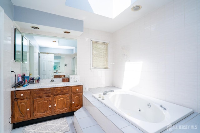 full bathroom with vanity, a skylight, tile patterned flooring, tile walls, and a jetted tub