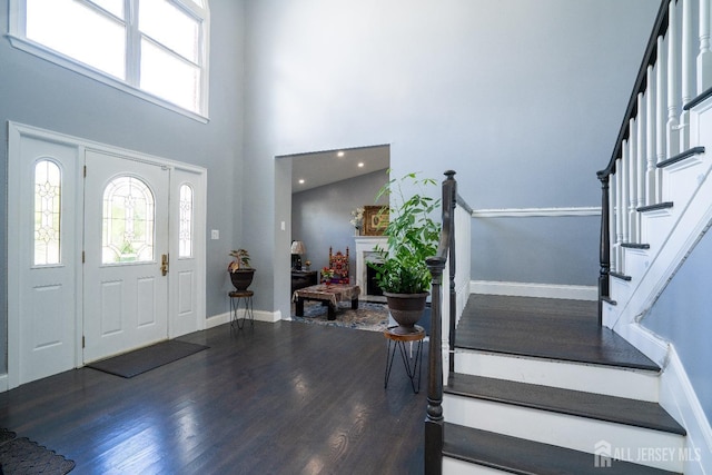 entryway with baseboards, stairs, a fireplace, a high ceiling, and wood finished floors