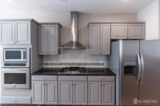 kitchen featuring gray cabinetry, decorative backsplash, appliances with stainless steel finishes, and wall chimney range hood
