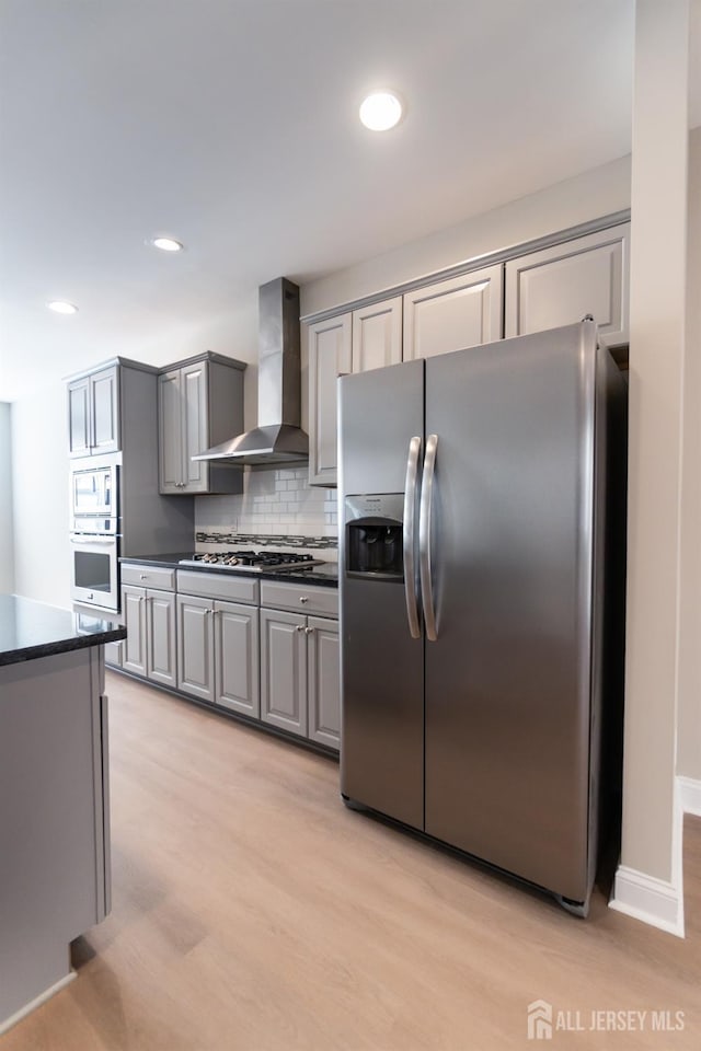 kitchen with dark countertops, wall chimney range hood, tasteful backsplash, appliances with stainless steel finishes, and gray cabinetry