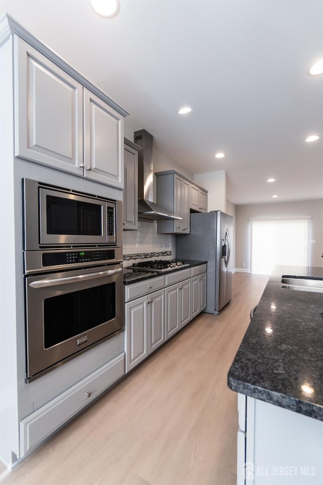 kitchen with wall chimney range hood, light wood-type flooring, recessed lighting, a sink, and appliances with stainless steel finishes