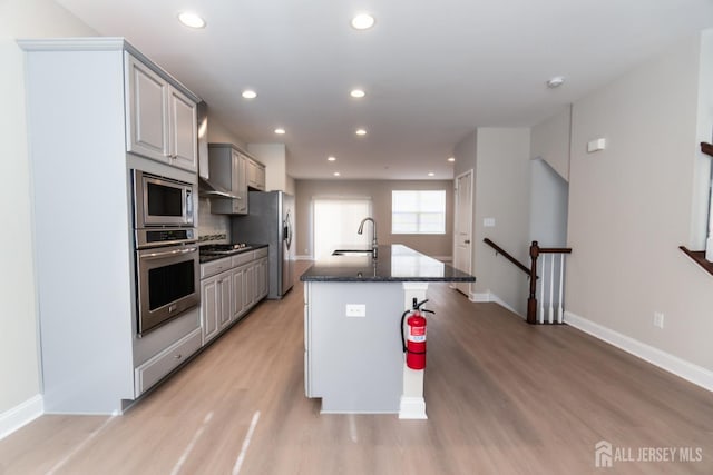 kitchen featuring light wood-type flooring, baseboards, appliances with stainless steel finishes, and a center island with sink