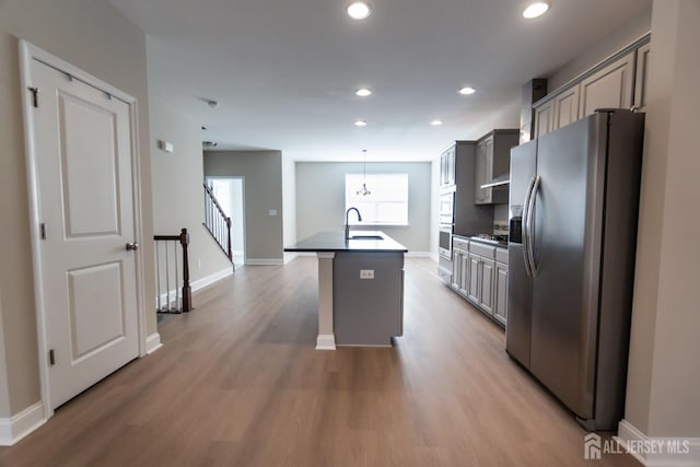 kitchen featuring a kitchen island with sink, stainless steel refrigerator with ice dispenser, gray cabinetry, and a sink