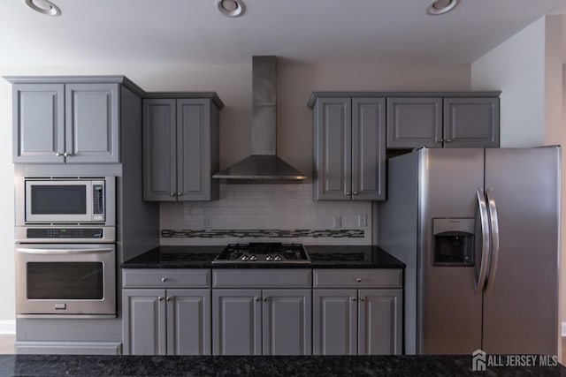 kitchen featuring wall chimney exhaust hood, dark stone countertops, backsplash, gray cabinetry, and stainless steel appliances