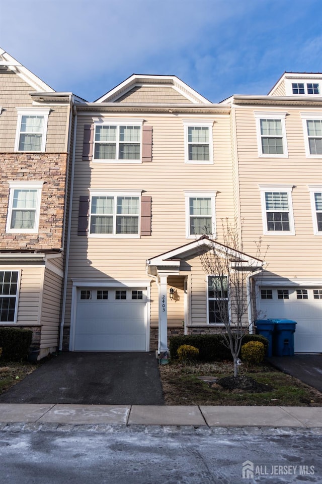 townhome / multi-family property with a garage, aphalt driveway, and stone siding