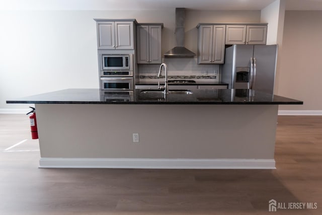 kitchen featuring wall chimney range hood, appliances with stainless steel finishes, baseboards, gray cabinetry, and dark wood-style floors