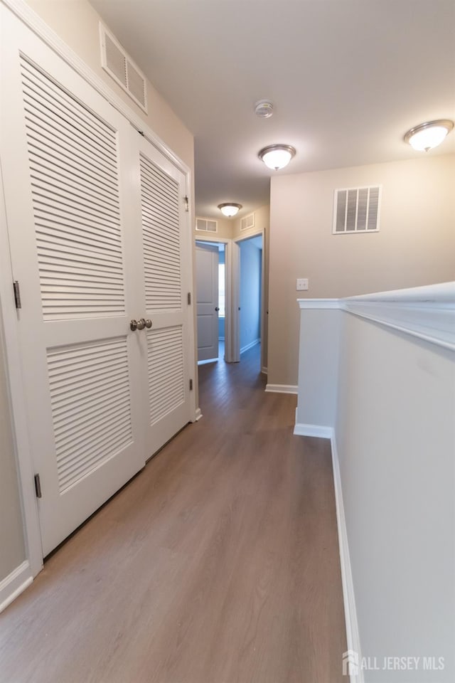 corridor featuring baseboards, visible vents, and wood finished floors