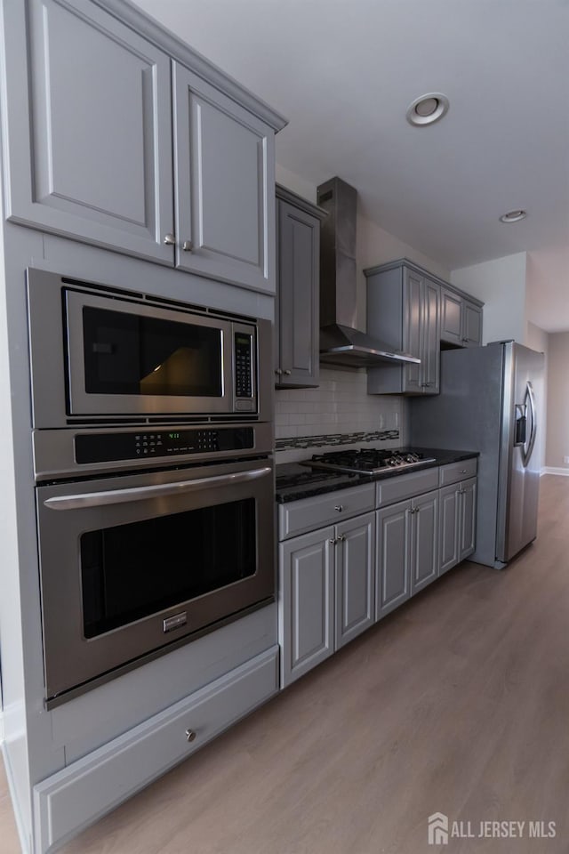 kitchen featuring wall chimney range hood, gray cabinets, stainless steel appliances, and light wood finished floors