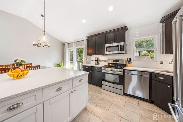 kitchen featuring appliances with stainless steel finishes, decorative light fixtures, vaulted ceiling, white cabinetry, and backsplash