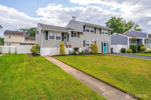 tri-level home featuring a chimney, fence, and a front lawn