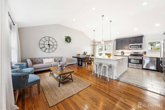 living area with a baseboard radiator, light wood-style floors, plenty of natural light, and vaulted ceiling