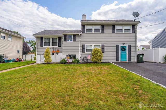 tri-level home featuring a chimney, fence, and a front lawn