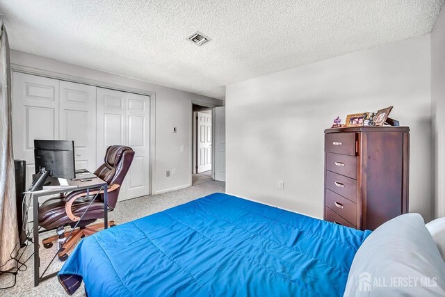 carpeted bedroom with a closet, a textured ceiling, baseboards, and visible vents