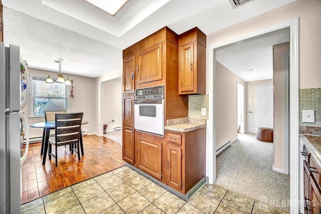 kitchen with oven, a notable chandelier, freestanding refrigerator, light tile patterned floors, and backsplash