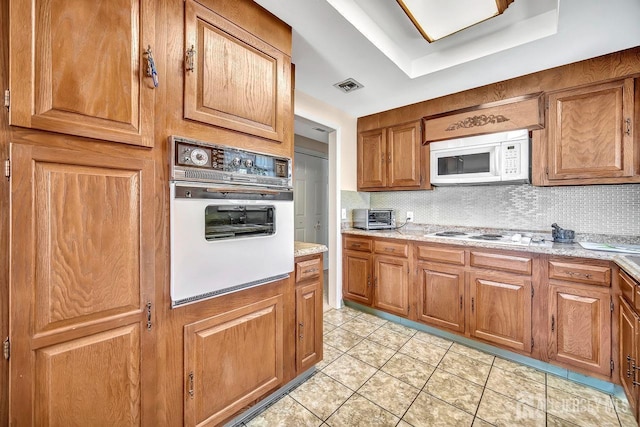 kitchen featuring visible vents, brown cabinetry, white appliances, tasteful backsplash, and light tile patterned floors