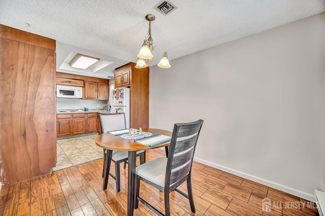 dining space with visible vents, a textured ceiling, light wood finished floors, and a notable chandelier