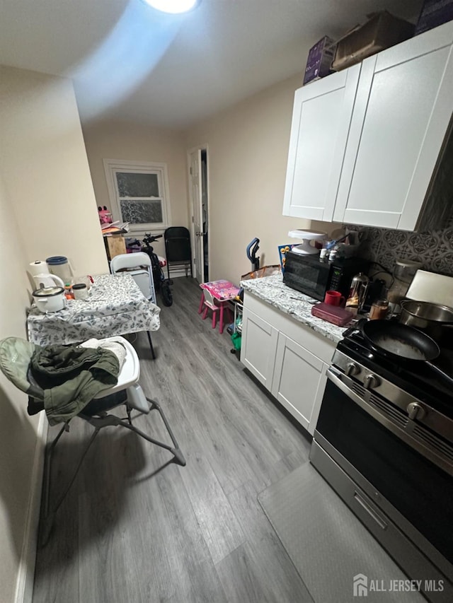 kitchen with light hardwood / wood-style flooring, light stone countertops, stainless steel range oven, and white cabinets