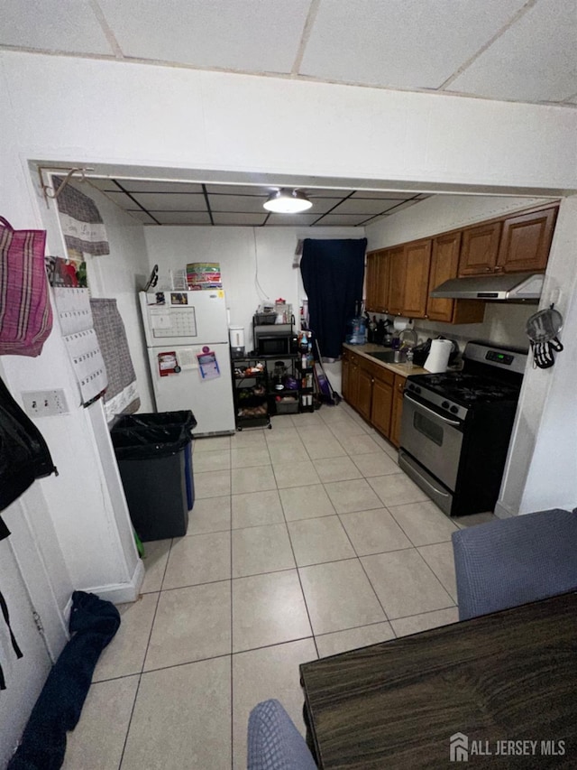 kitchen featuring white fridge, light tile patterned floors, a drop ceiling, and stainless steel gas stove