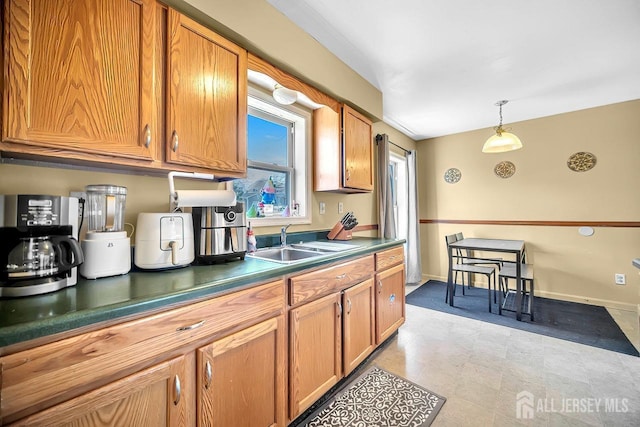 kitchen featuring dark countertops, baseboards, decorative light fixtures, brown cabinets, and a sink