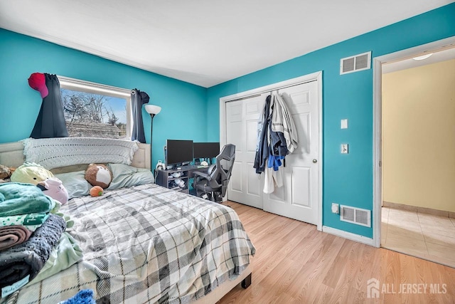 bedroom with wood finished floors, visible vents, a closet, and baseboards