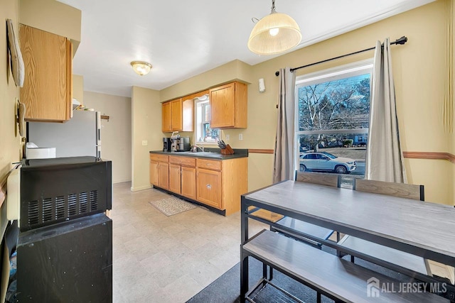 kitchen featuring dark countertops, light floors, pendant lighting, freestanding refrigerator, and a sink