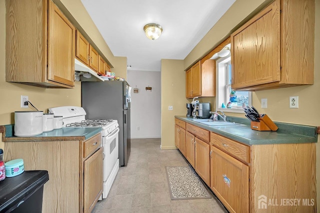 kitchen featuring baseboards, a sink, white gas range oven, under cabinet range hood, and dark countertops