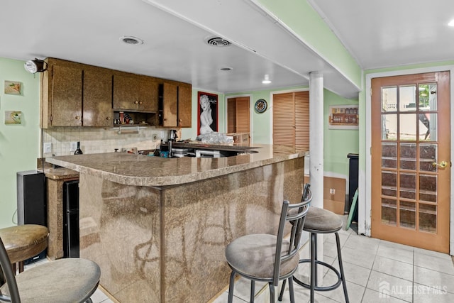 kitchen featuring a breakfast bar, tasteful backsplash, visible vents, light tile patterned flooring, and a peninsula