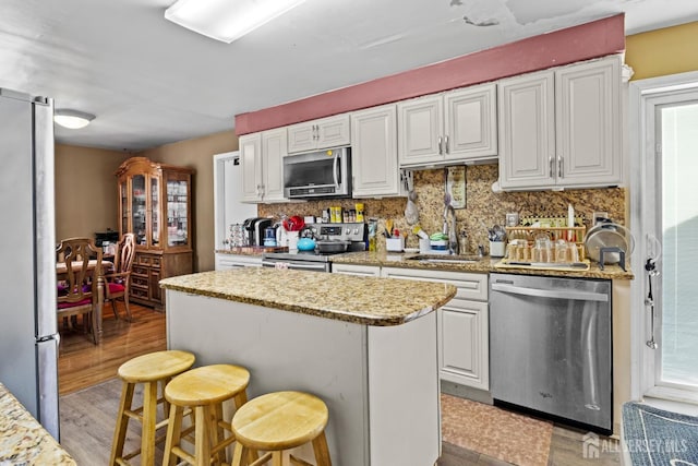 kitchen with a kitchen island, a sink, appliances with stainless steel finishes, backsplash, and light wood finished floors