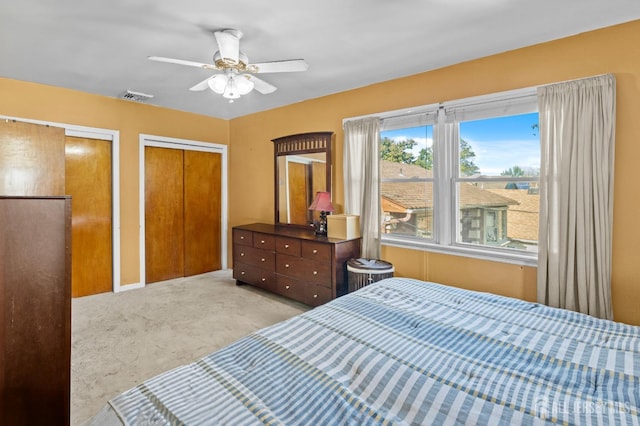 bedroom featuring light carpet, ceiling fan, visible vents, and multiple closets